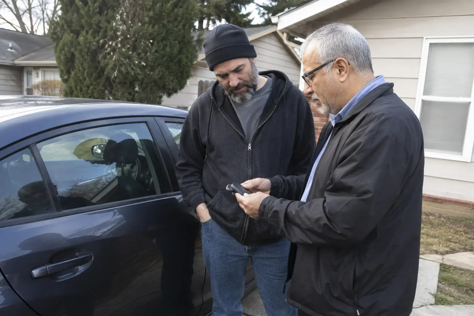Two adults discussing a key fob beside a parked car. — Car Lockout Service, Norfolk County