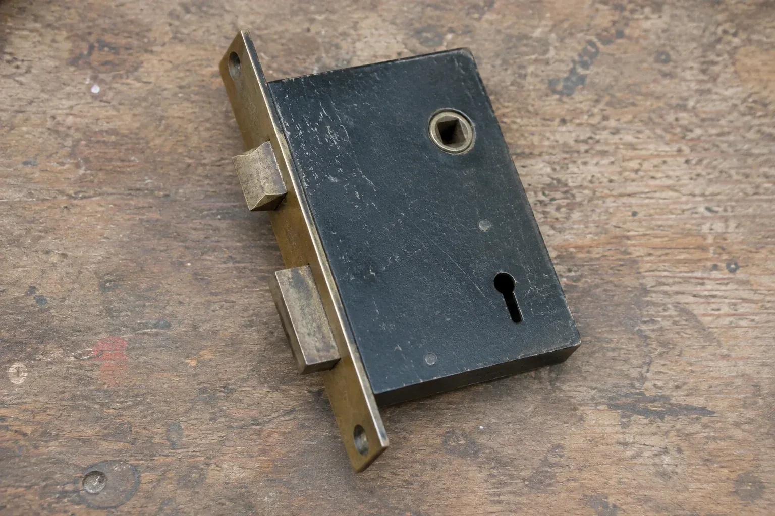 Closed mortise lock case with spindle opening, keyhole, latch and deadbolt on a wooden workbench. — Vintage Mortise Lock Service, Norfolk County