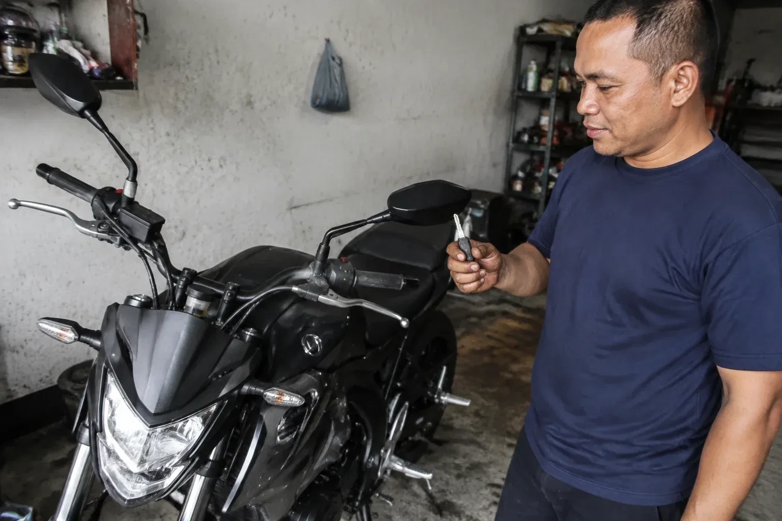 Person holding a key beside a black motorcycle in a garage. — Motorcycle & Scooter Keys, Norfolk County