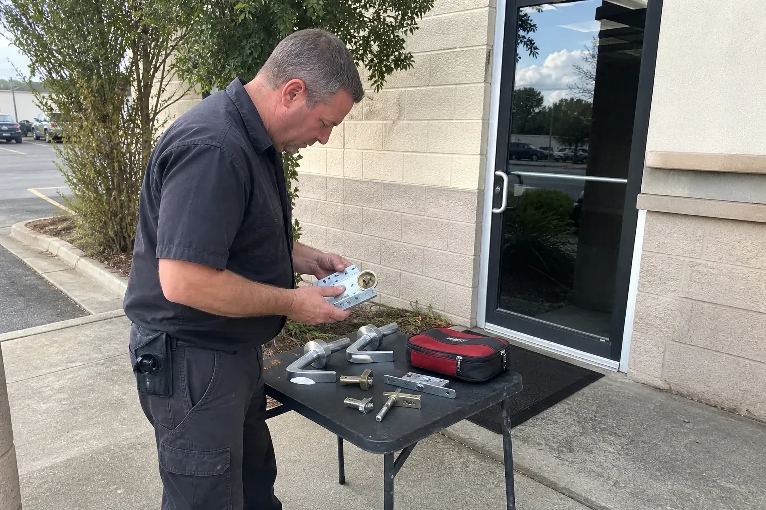Technician examining detached commercial lock hardware on a table outside a shop entrance. — Business Lockout Service, Norfolk County